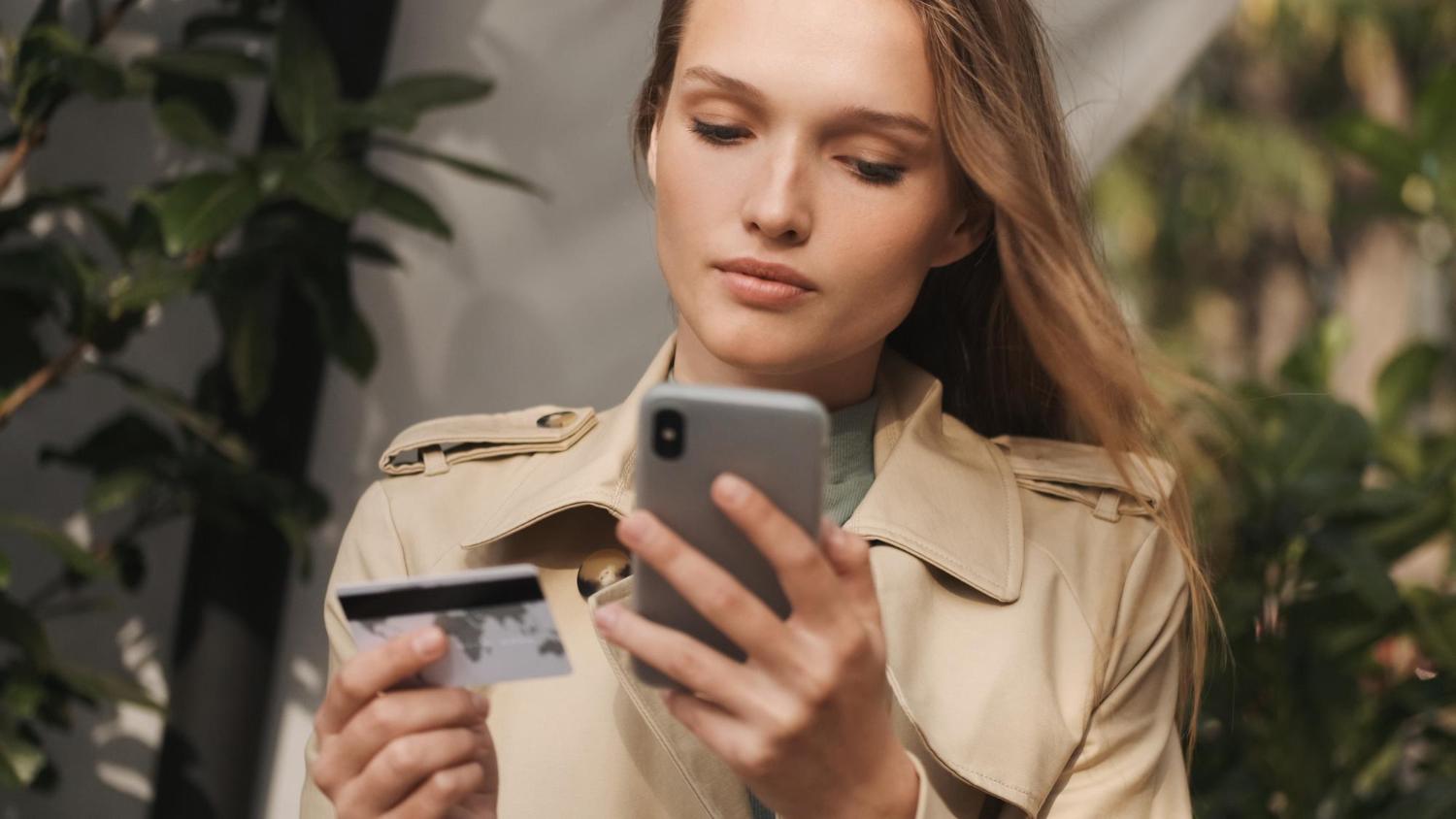 young woman using banking app on her mobile phone and keeping a credit card in her hand